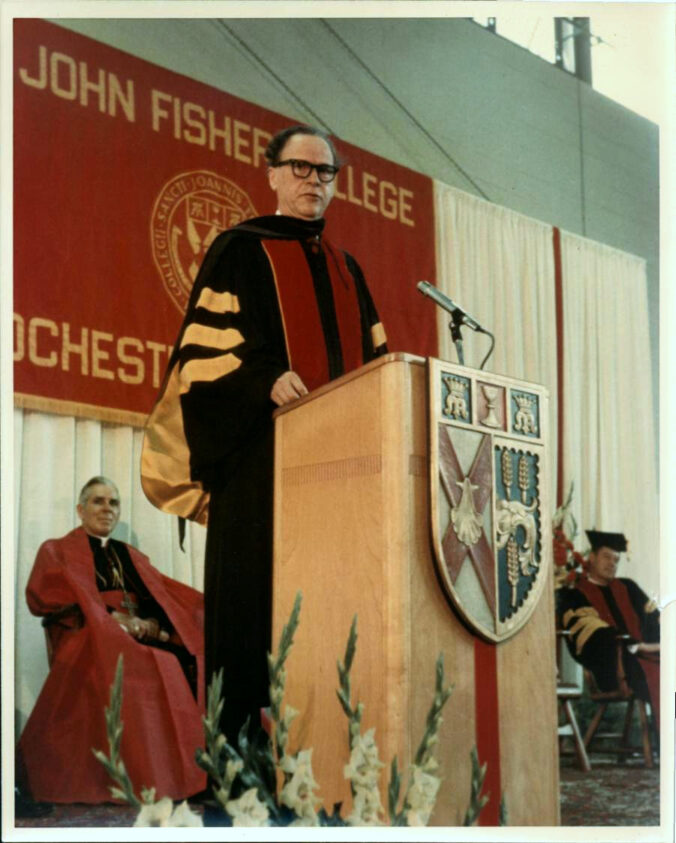 Marshall McLuhan at the podium at John Fisher College. Fulton Sheen sits in the background.